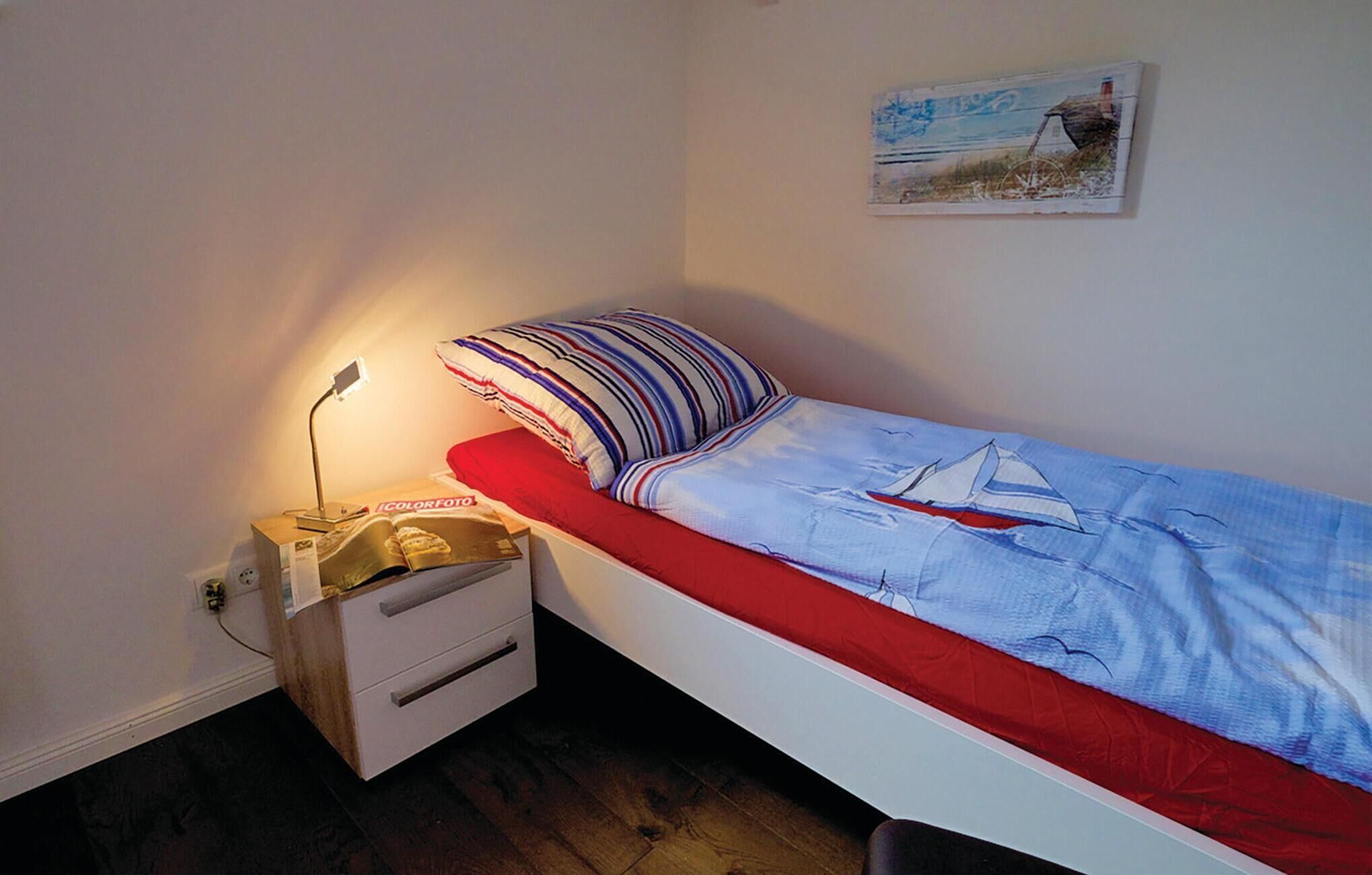 Una stanza piccola con un letto singolo, un comodino in legno, una lampada e una rivista.
