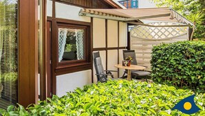 Een huis met een overdekt terras, een raam met kantgordijnen en een kleine tafel met stoelen.