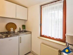 Una cocina compacta con estufa, pileta y ventana con cortina.