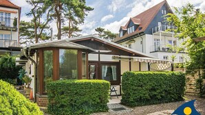 Een woongebouw met een overdekte veranda, een kleine tuin met hagen en uitzicht op omliggende huizen.