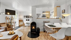 Uma sala de estar moderna com lareira, paredes brancas, piso de madeira e um espaço de jantar com cadeiras brancas.