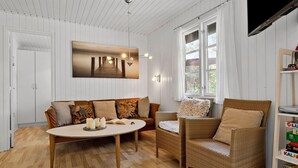 Um quarto aconchegante com piso de madeira, uma mesa redonda com velas, um sofá e duas cadeiras de vime.