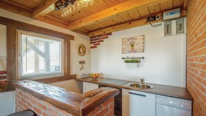 Een keuken met een stenen aanrecht, een spoelbak en een vaatwasser. Er is een raam met zonwering, een klok en een bord aan de muur.