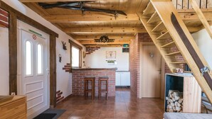 Een rustiek interieur met een metselwerk open haard, houten balkenplafond, een keukenhoek en een trap.