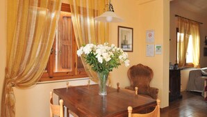 A dining area with a wooden table, chairs, a vase with white flowers, and a hanging light fixture. - Holiday apartment mit Pool (Vicchio)