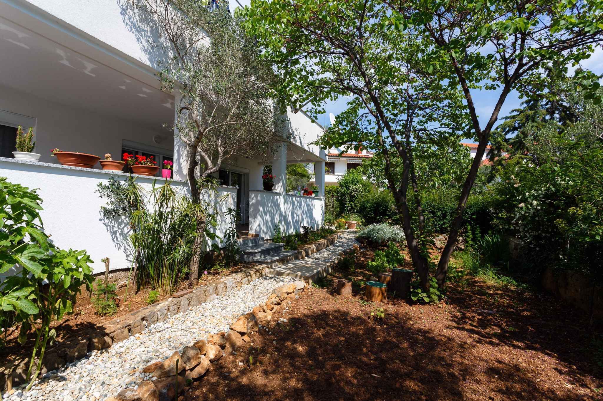 A white building with a covered outdoor area, stone steps, and a garden with various plants and a tree.