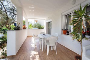 A covered outdoor patio with a table and chairs, surrounded by potted plants and a view of the street. - Holiday apartment with air conditioning (Krk)