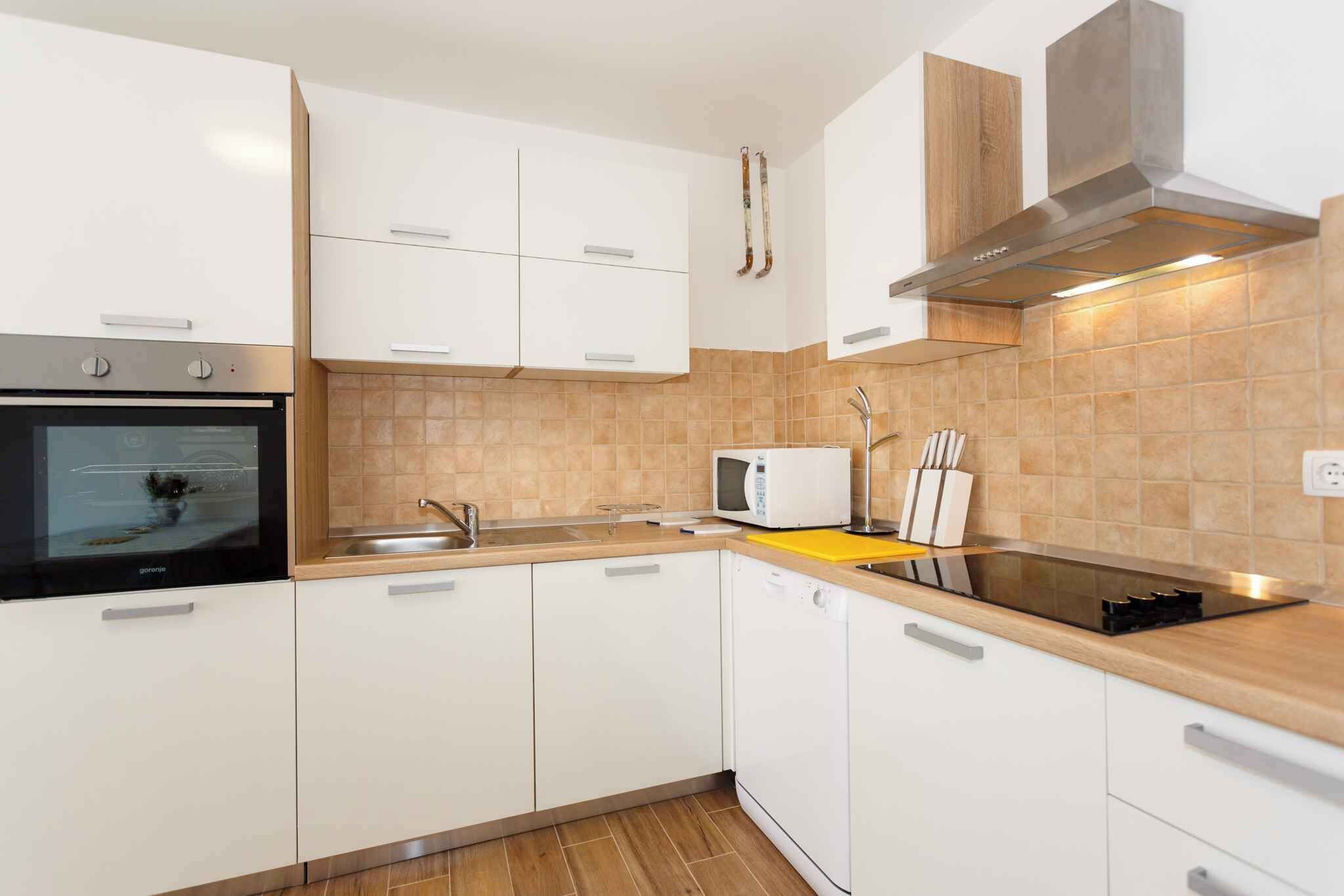 Een moderne keuken met witte kastjes, een inbouwoven, een magnetron, een spoelbak en een rvs-afzuigkap.