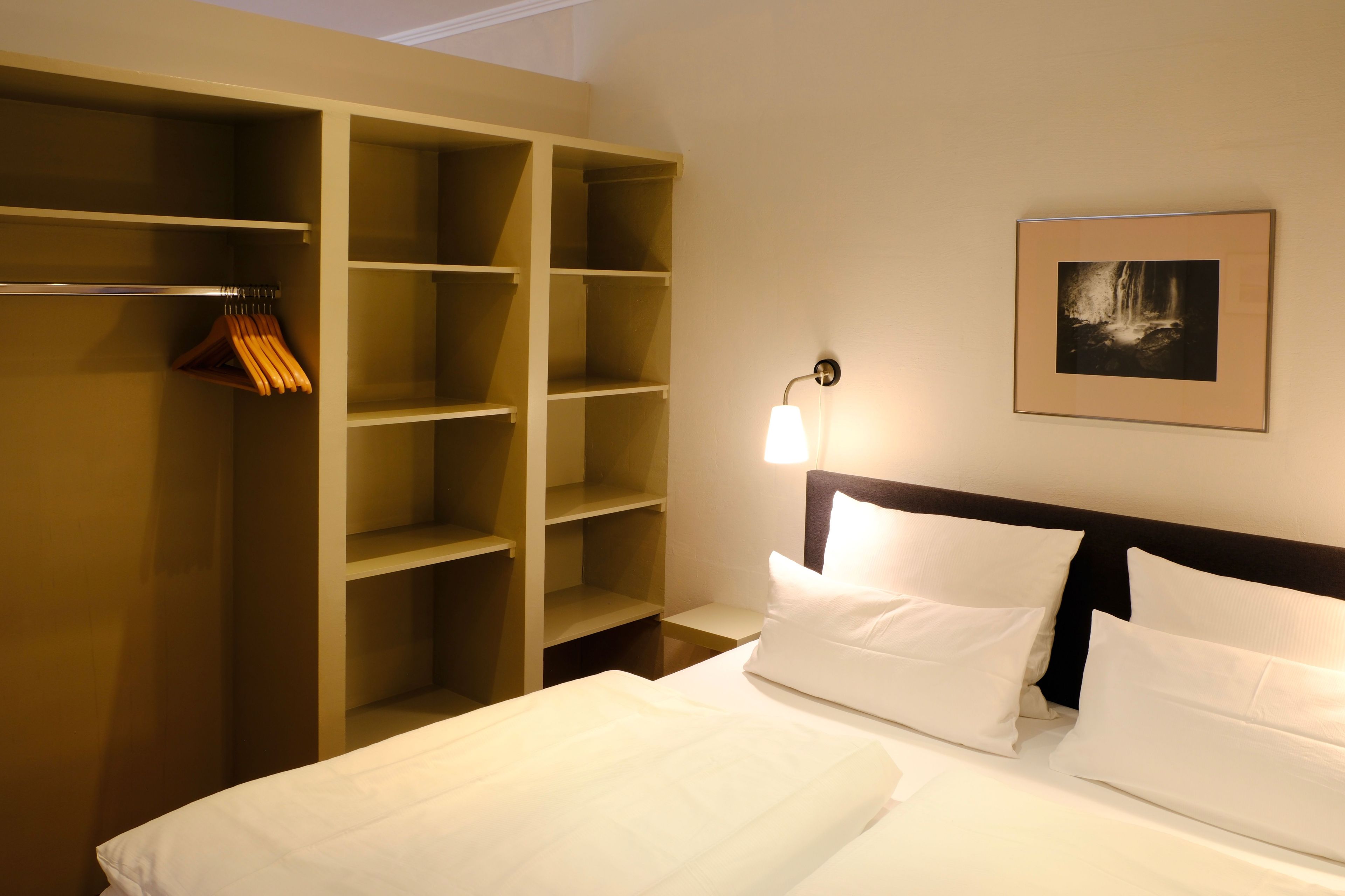 A hotel room with a bed, a wardrobe, a nightstand, and a framed picture on the wall.