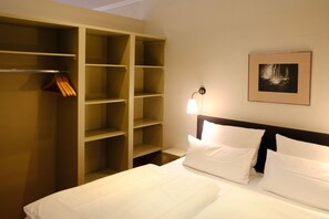 A hotel room with a bed, a wardrobe, a nightstand, and a framed picture on the wall.