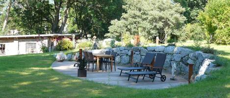 Un patio con un muro de piedra, una mesa de madera y sillas.