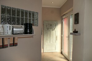 A kitchen with a coffee maker, toaster, and kettle on a shelf, a door with a frosted glass panel, and a small shelf with a decorative item.