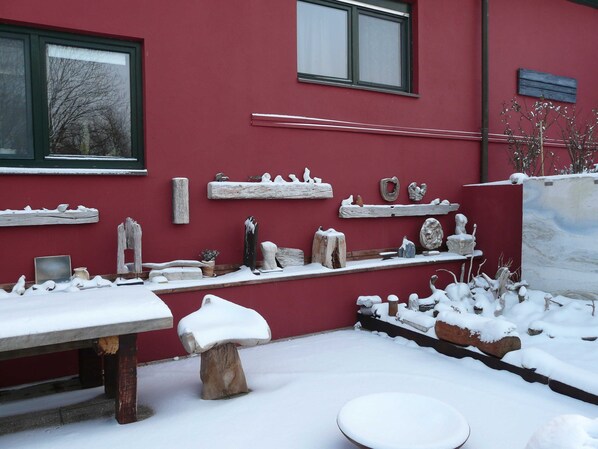 A red building with multiple windows, outdoor seating, and various sculptures and decorations.