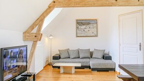 A cozy loft bedroom with a wooden ceiling, a gray sofa, a white door, and a painting of a snowy landscape. - 2 bedroom amazing apartment in Ponts (Ponts)