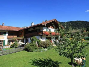 Un bâtiment à deux étages, doté d’un toit en pente, d’une cour clôturée et avec une montagne en arrière-plan.