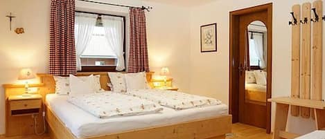 A bedroom with a wooden bed, two bedside tables with lamps, a window with curtains, a mirror, and a wooden chair.