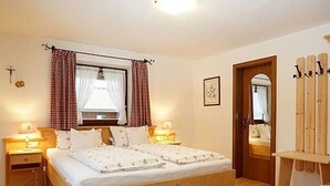 Une chambre à coucher avec un lit en bois, deux tables de chevet avec des lampes, une fenêtre avec des rideaux, un miroir et une chaise en bois.
