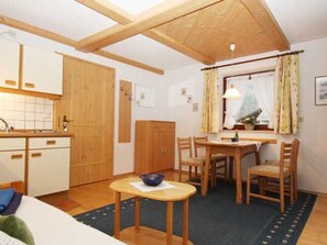 Ein gemütliches Zimmer mit Holzboden, einem Esstisch mit Stühlen, einem kleinen Tisch mit einer Schale und einem Fenster mit Vorhängen.