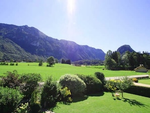 Paisaje rural con un campo verde, un edificio pequeño y montañas al fondo.