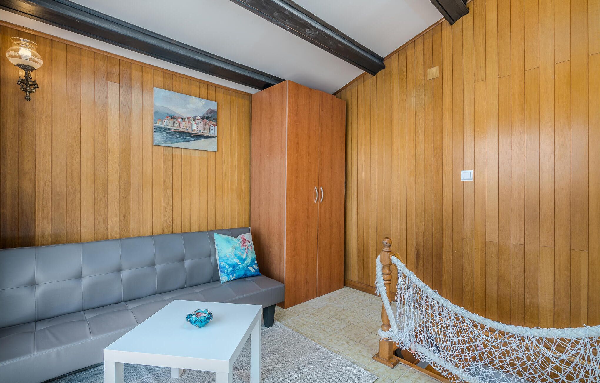 A room with a grey sofa, a white coffee table, wooden panel walls, a painting, and a hammock.