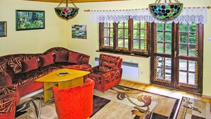 A living room with a red sofa, a red armchair, a yellow coffee table, and a patterned rug. There are two wall-mounted lamps and a window with decorative glass panes.