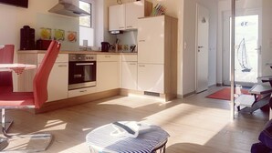 Cozinha moderna com fogão, forno e armários. Há uma área de jantar com mesa e cadeiras.