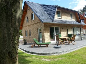 Une maison à deux étages, avec un toit en tuiles, une façade en briques et un patio aménagé avec du mobilier d’extérieur.