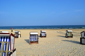 Des chaises de plage sont alignées sur une plage de sable, avec l’océan en arrière-plan.