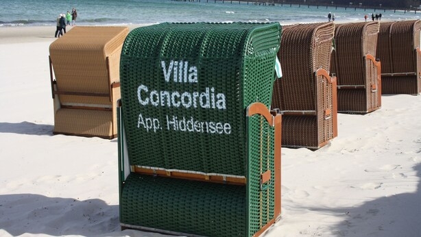 Eine Reihe von Strandhäusern mit der Aufschrift "Villa Concordia" und einem Schild, das auf eine App für Reservierungen hinweist.