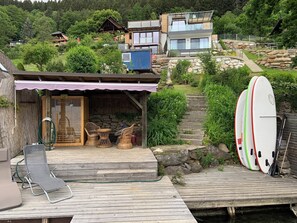 A wooden deck with a covered seating area, a stone staircase, and a row of surfboards.
