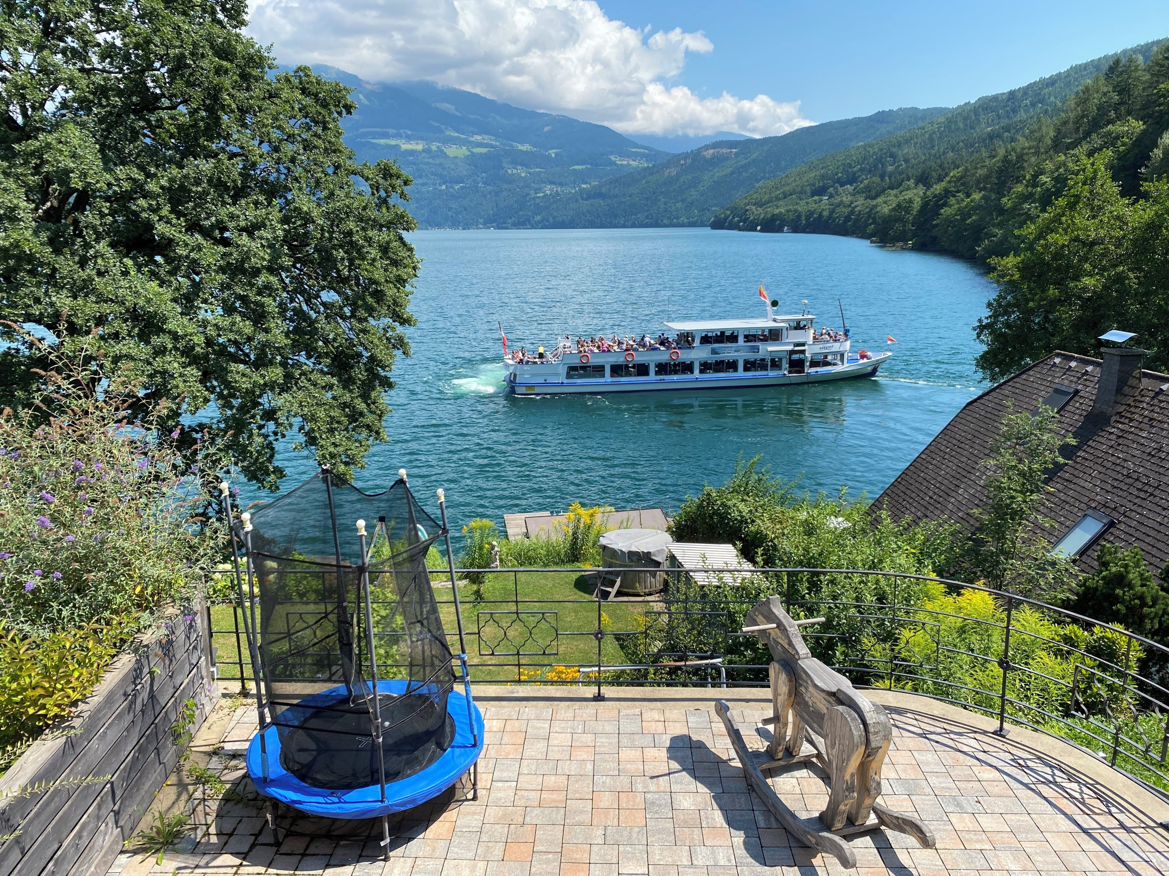 A view of a lake with a boat, a trampoline, and a wooden sculpture.