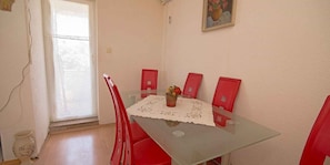 A dining area with a glass table, red chairs, a lace tablecloth, and a vase with flowers.