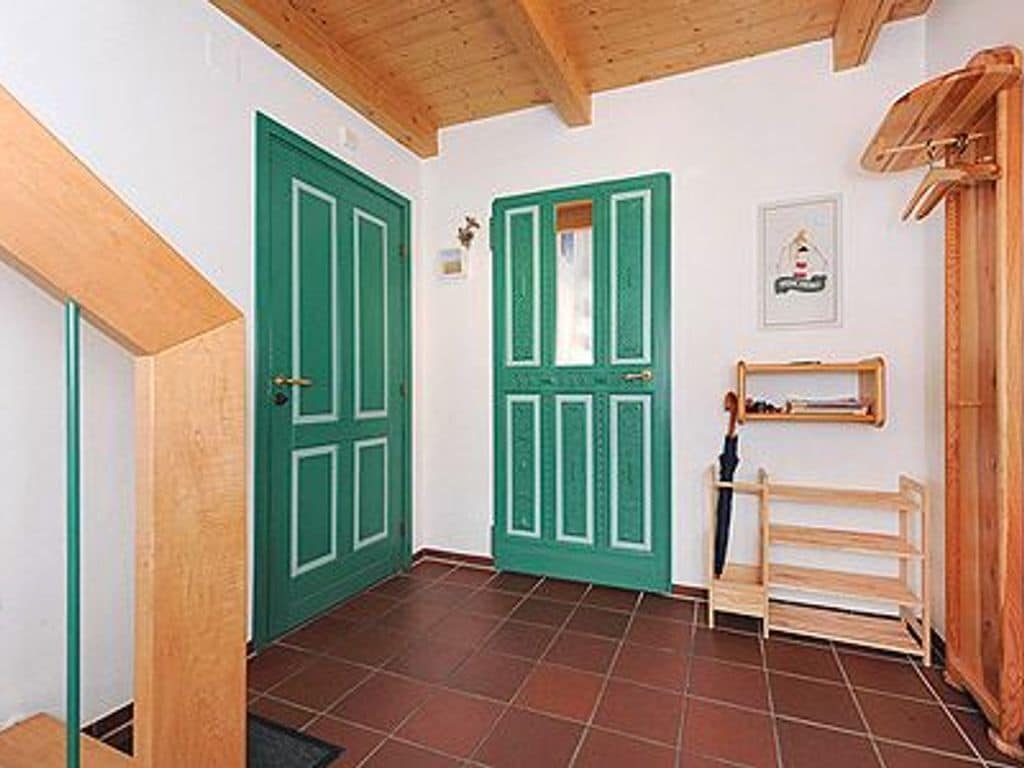 Un couloir avec des portes vertes, un banc en bois et un tableau encadré accroché au mur.