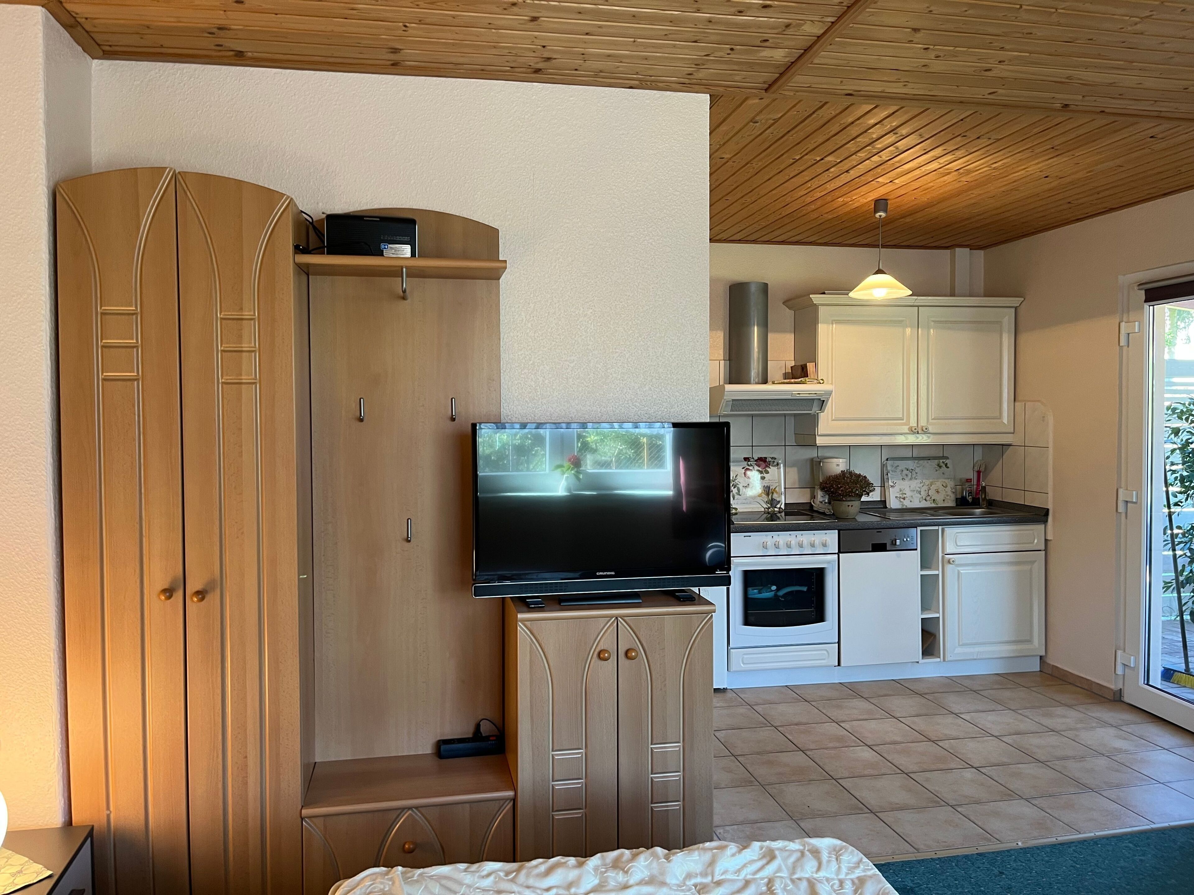 Ein gemütlicher Wohnbereich mit Küchenzeile, einem Fernseher auf einem Holzschrank und einem Bett mit einem grünen Teppich.