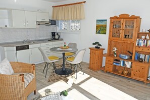Una cocina con armarios blancos, una mesa de comedor con sillas, una máquina de café y un aparador de madera con puertas de vidrio.