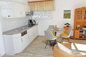 Una cocina compacta con armarios blancos, cafetera y comedor con una mesa redonda y dos sillas.
