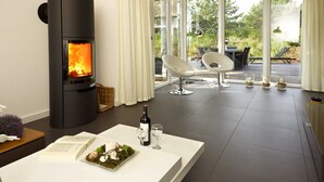 Un soggiorno moderno con stufa a legna, angolo pranzo con tavolo bianco e vista sull'esterno.