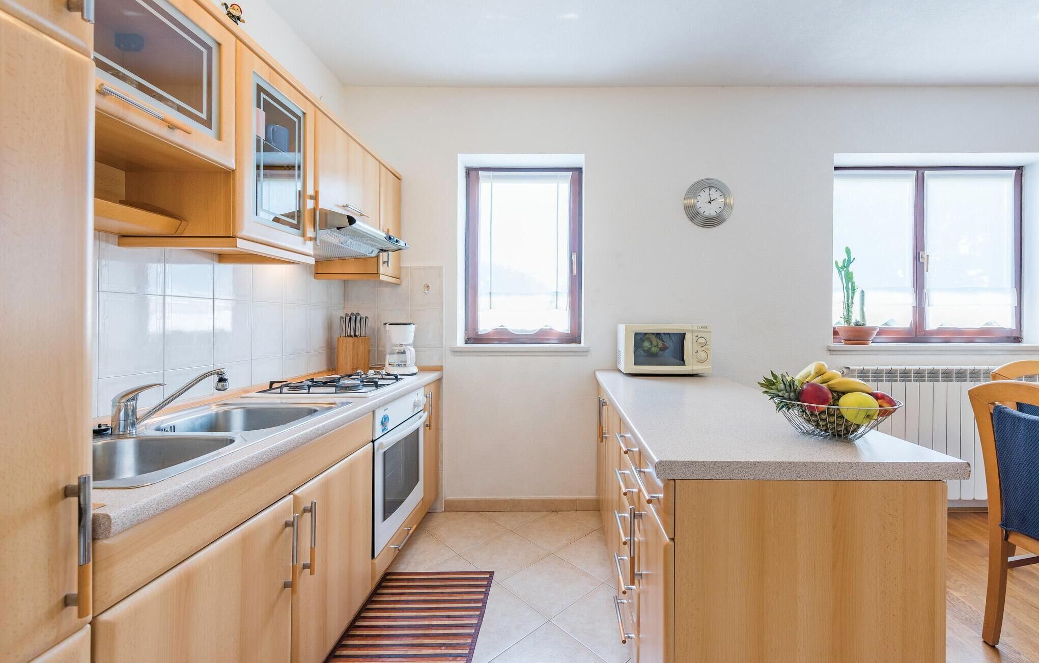 A modern kitchen with wooden cabinets, a gas stove, a microwave, and a fruit bowl on the island.