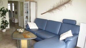 A living room with a blue sofa, a coffee table, and a decorative feather. - (257) 3-room apartment - apartment complex holiday dreams (Kühlungsborn)