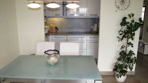 A modern kitchen with white cabinets, a glass dining table, and pendant lighting. - (257) 3-room apartment - apartment complex holiday dreams (Kühlungsborn)