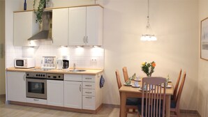 Cocina compacta con armarios blancos, microondas, cafetera y mesa de comedor con sillas.