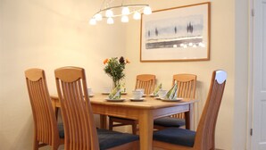 Un comedor con una mesa y sillas de madera, un jarrón con flores y un cuadro en la pared.