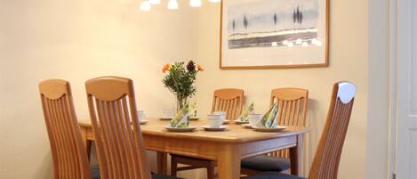 A dining area with a wooden table and chairs, a vase with flowers, and a framed picture on the wall.