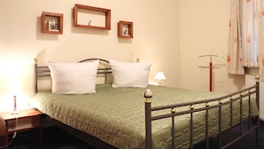 Una cama individual con colcha verde, dos mesitas de noche con lámparas, y tres cuadros enmarcados en la pared.