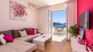 A modern living room with a sofa, a coffee table, and a TV on a stand. There is a balcony with a view of the sea and a table with chairs. - Cozy apartment in Zaton Mali (Zaton Mali)
