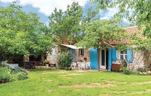 Ein Haus aus Stein mit blauen Fensterläden, einer Steintreppe und einem kleinen Garten mit Tisch und Stühlen.