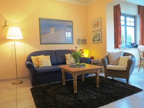 Un salon avec un canapé bleu foncé, une table basse en bois sur laquelle est posé un vase de fleurs, un lampadaire et un tableau accroché au mur.