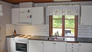 Cozinha compacta com armários brancos, fogão, forno, pia e janela com vista para o verde.