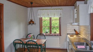 Cozinha compacta com teto de madeira, uma janela com vista para o verde, fogão e área de refeições com cadeiras e mesa.