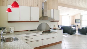 Une cuisine moderne avec des meubles blancs, un plan de travail en granit, un évier en acier inoxydable et des suspensions rouges.